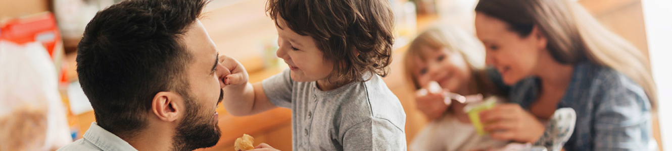 Father and child smiling together as they play and mother feeding other child and smiling. 